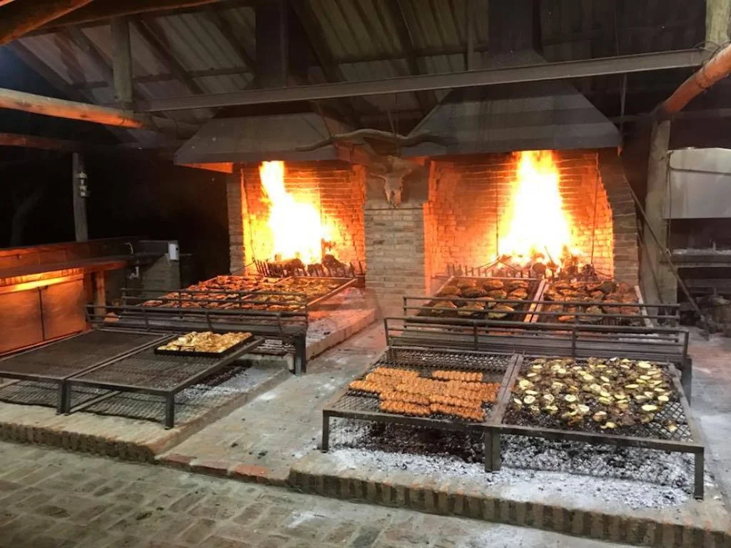 Parrilla llena de carne y chorizos asándose en Rafaella ChacraEventos, lista para una deliciosa cena